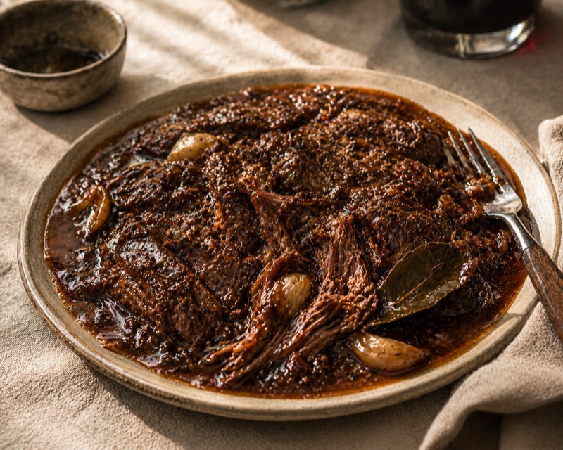 Sukadelapjes in donkere bier-uienjus met knoflook en laurier op crème linnen