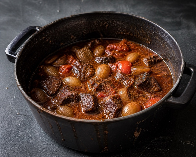 Stoofvlees met bier in een gietijzeren pot met sjalotjes en tomaten