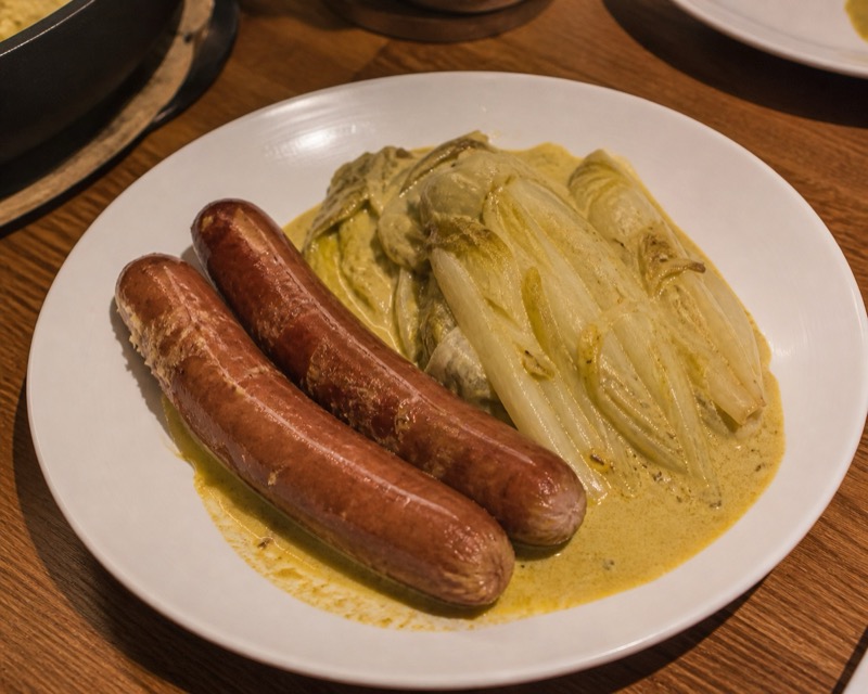 Rundersaucijsjes met gestoofde andijvie in kerriesaus op een wit bord