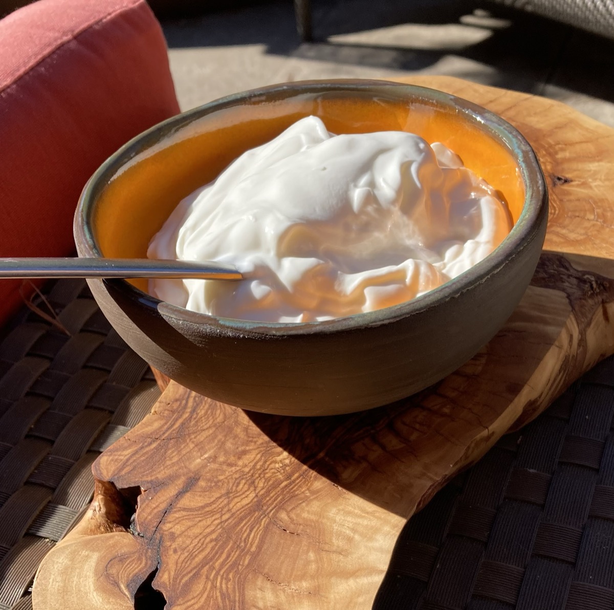 Kom met volle joghurt en vruchtenpuree op een olijfhouten plank, buiten in de zon — een voorbeeld van het dagelijkse zuiveladvies.